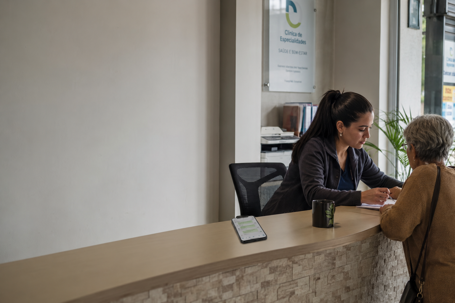 Recepcionista de cl�ínica atendendo pessoalmente uma paciente idosa no balcão, enquanto o celular ao lado mostra conversas de WhatsApp sendo resolvidas pelo agente.